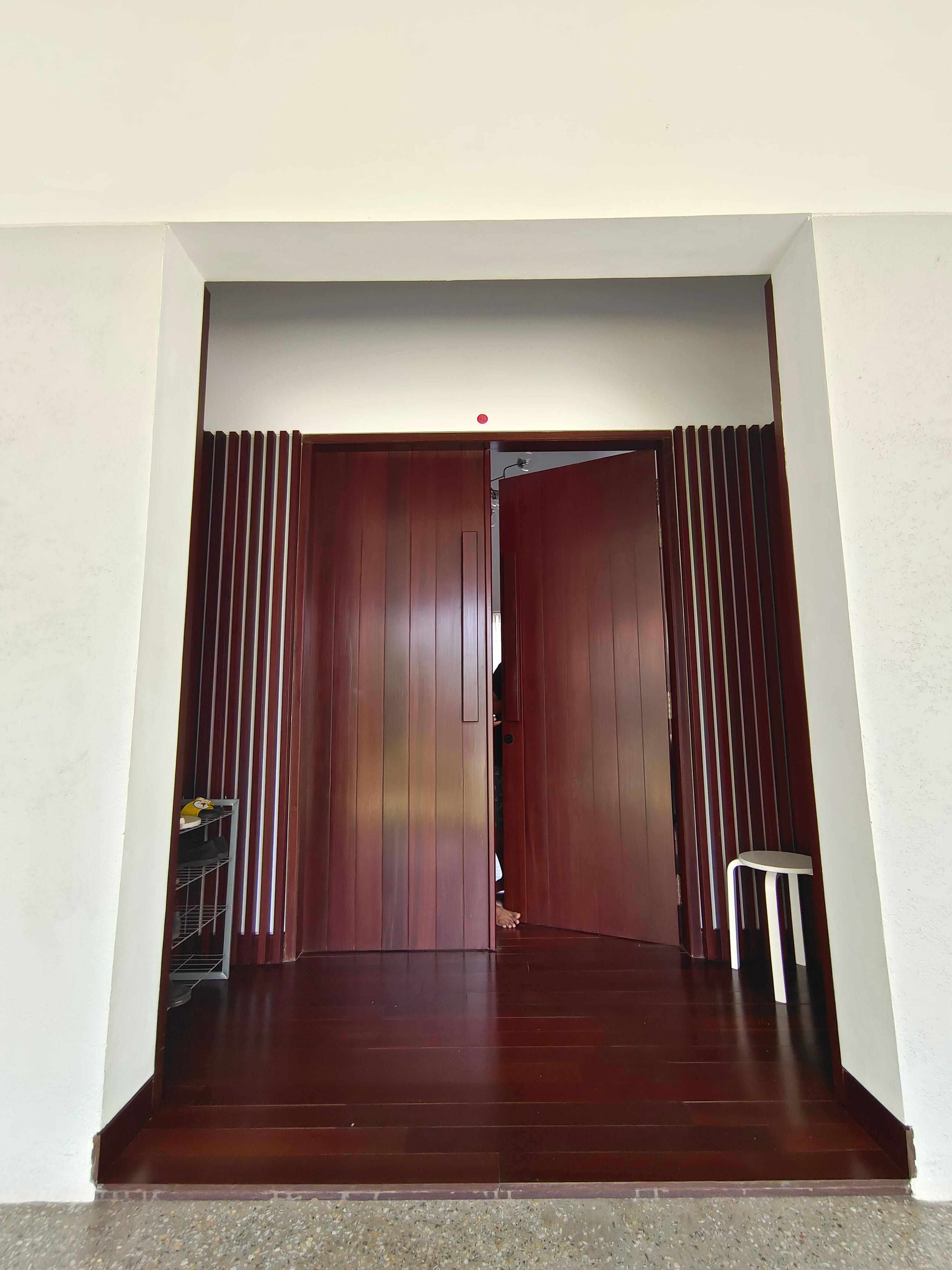 Custom solid wood pivot door with flanking kisi-kisi columns and dark hardwood strip flooring at Kowi Bangka by Reywood